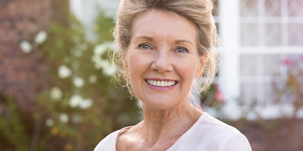 elderly woman standing out side her house smiling at camera